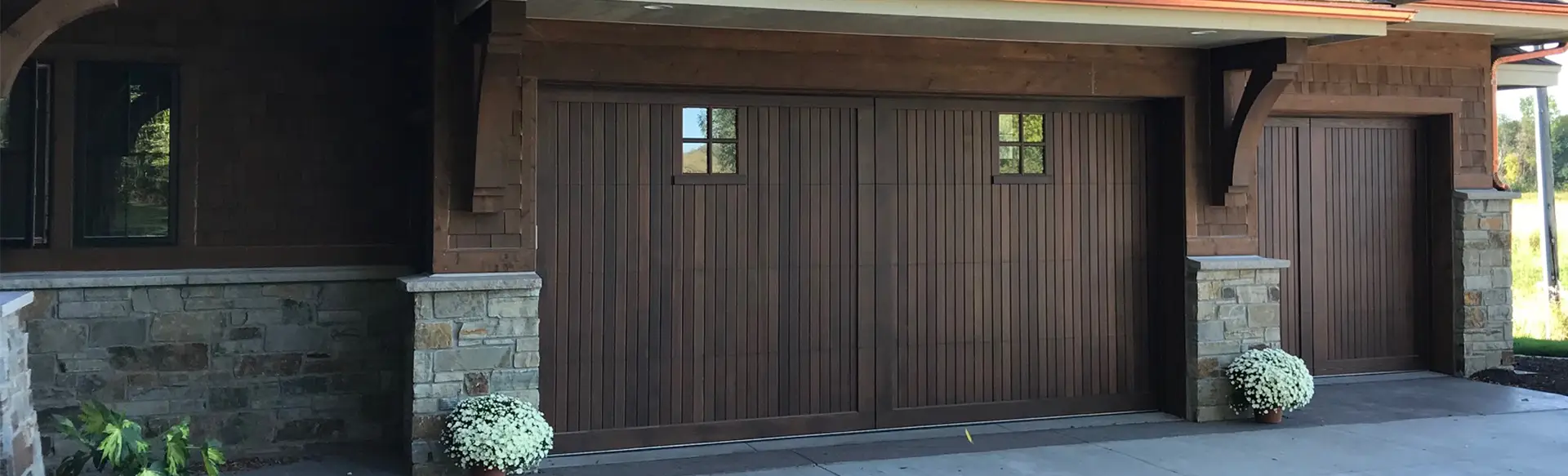 Dark stained wood garage door with a handcrafted design, creating a warm and elegant entrance.
