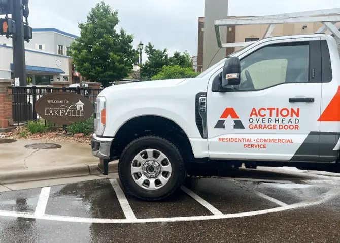 A white Action Overhead service truck is parked near stoplight in historic downtown getting ready for a garage door repair in Lakeville