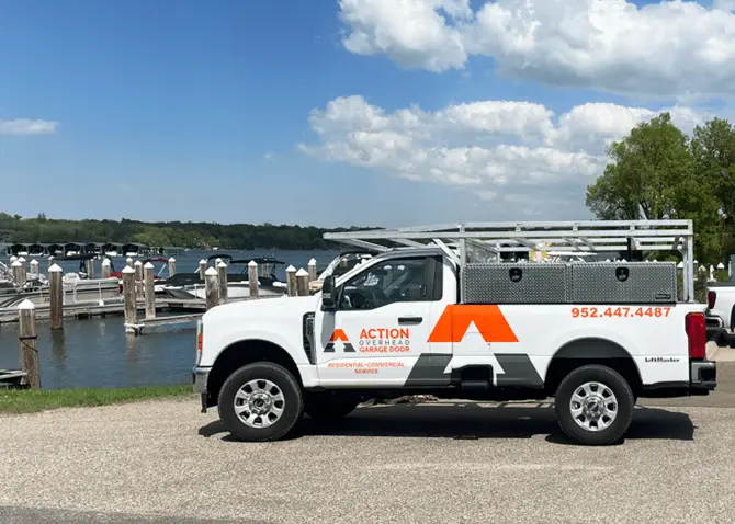 An Action Overhead pick-up truck is parked outside of a small marina getting ready for a garage door repair in Minnetonka. Boats are moored to the docks on a sunny summer day.
