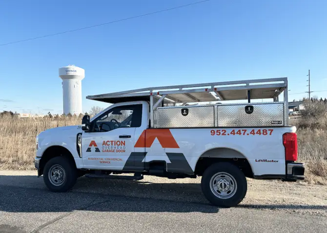 An Action Overhead service truck is seen parked near an open field getting ready for a garage door repair in Shakopee.. The municpal water tower is seen in the background against a bright sky with swirling clouds.
