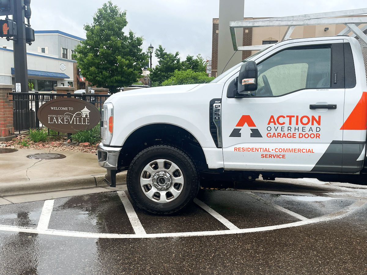 A white Action Overhead service truck is parked near stoplight in historic downtown getting ready for a garage door repair in Lakeville